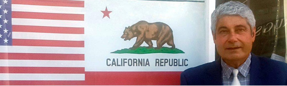 Mahmoud Shirazi in front of flags and the California Republic banner